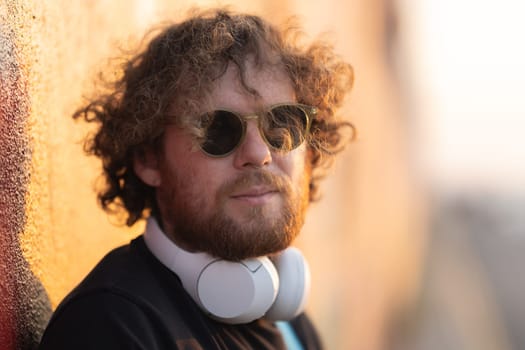 Romantic man with curly hair wearing wireless headphones at sunset. Portrait
