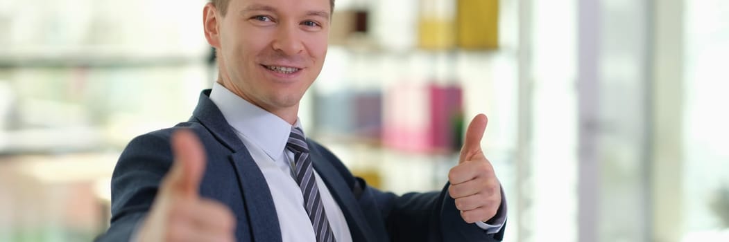 Happy smiling businessman showing thumbs up gesture in office. Successful career growth in business concept