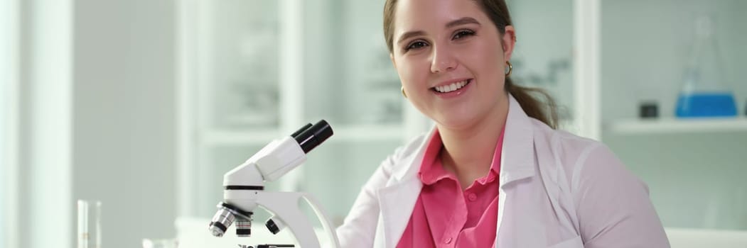 Portraits of smiling woman chemist in front of microscope in lab. Laboratory diagnostics of human diseases concept