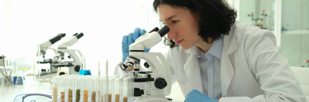 Man agronomist breeding new plant variety and looking through microscope in lab. Selection and genetically modified food concept