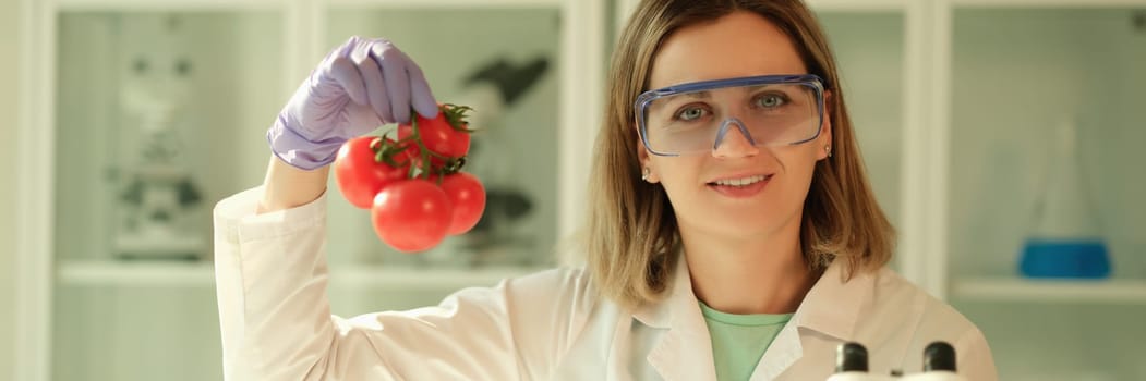 Scientist chemist in protective glasses holding branch of tomatoes in hands in chemical laboratory. Genetically modified food production concept