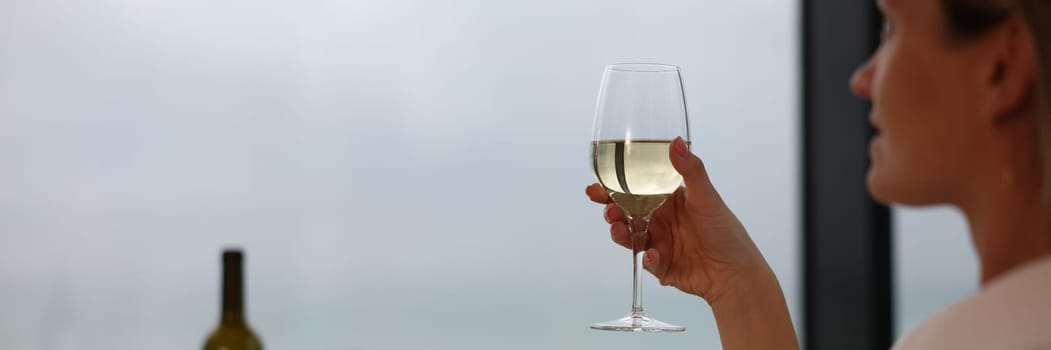 Woman in bathrobe holding glass of white wine closeup. Rest and relaxation in hotel concept