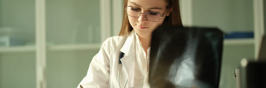 Doctor pulmonologist examining x-ray lungs and writing patient medical history in clinic. Xray diagnosis of pneumonia concept