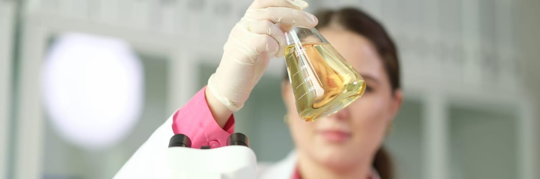 Scientist chemist looking at flask with yellow liquid or oil for transparency in chemical laboratory closeup. Machine oil quality control concept