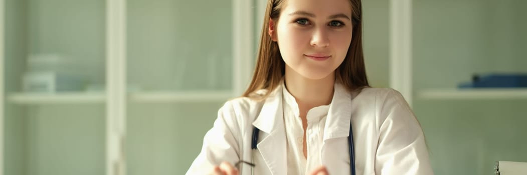 Portrait of young woman doctor with glasses in her hands in clinic. Healthcare and medicine concert