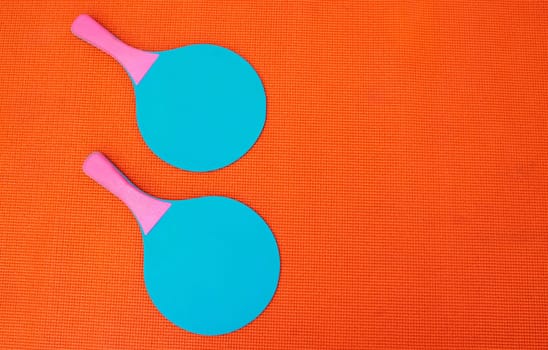 I need a partner. High angle shot of two table tennis bats placed together on top of an orange background inside of a studio