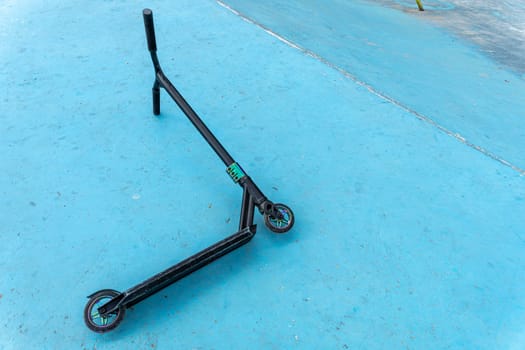 a stunt scooter, a modern extreme stunt scooter in a skate park lies on a concrete path. the scratched scooter lies after falling to the ground. The concept of a healthy lifestyle and sports leisure