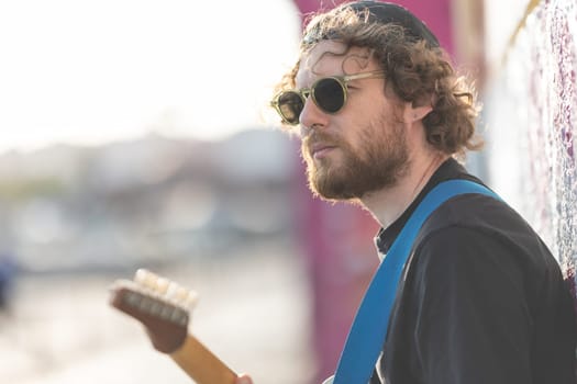 Brooding hipster man playing guitar on the street. Mid shot