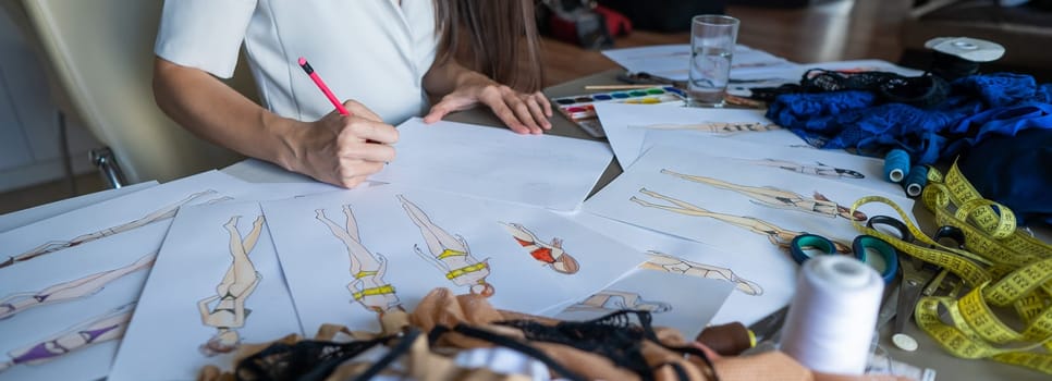 Faceless woman draws sketches of swimwear with a pencil. Close-up of the hands of a fashion designer