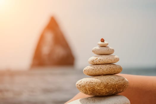 Woman bilds stones pyramid on the seashore on a sunny day on the blue sea background. Happy holidays. Pebble beach, calm sea, travel destination. Concept of happy vacation on the sea, meditation, spa