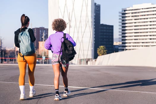 rear view of two unrecognizable friends walking along a city ready to run in a sunny day, concept of friendship and urban sport, copy space for text