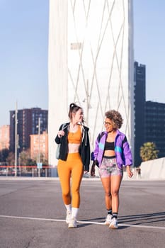 vertical photo of two women with sports clothes walking along the city, concept of friendship and urban sport, copy space for text