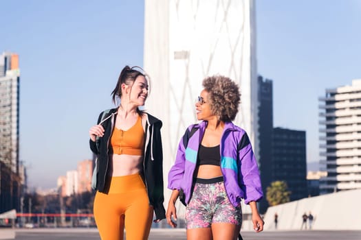 two women in sportswear talking while walking along the city, concept of friendship and urban sport, copy space for text