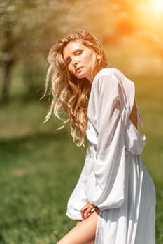 Blond blooming garden. A woman in a white dress walks through a blossoming cherry orchard. Long dress flies to the sides