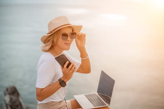 Freelance women sea working on the computer. Good looking middle aged woman typing on a laptop keyboard outdoors with a beautiful sea view. The concept of remote work