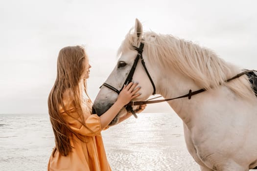 A woman in a dress stands next to a white horse on a beach, with the blue sky and sea in the background