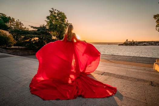 Sunrise red dress. A woman in a long red dress against the backdrop of sunrise, bright golden light of the sun's rays. The concept of femininity, harmony