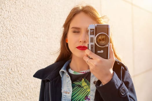 Outdoor autumn smiling lifestyle portrait of pretty young woman, having fun in the city with camera, travel photo of photographer. Making pictures in hipster style. Sun flare