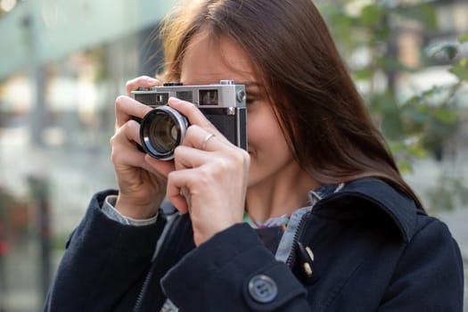 Outdoor autumn smiling lifestyle portrait of pretty young woman, having fun in the city with camera, travel photo of photographer. Making pictures in hipster style.