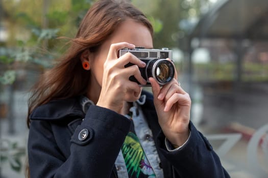 Outdoor autumn smiling lifestyle portrait of pretty young woman, having fun in the city with camera, travel photo of photographer. Making pictures in hipster style.