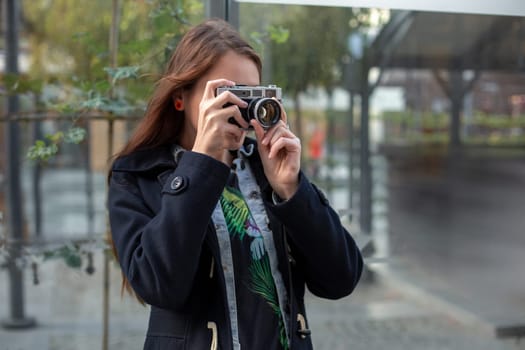 Outdoor autumn smiling lifestyle portrait of pretty young woman, having fun in the city with camera, travel photo of photographer. Making pictures in hipster style.