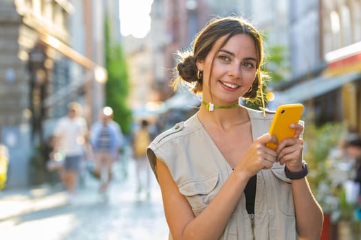 Tourist traveler pretty young woman using smartphone typing text messages looking for search a way on map in mobile navigator app outdoors. Girl walking passes by urban sunshine city street background