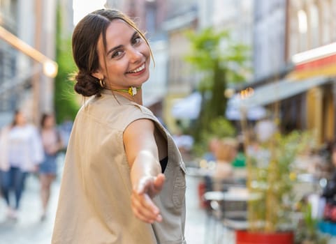 Rear view of pretty young woman tourist walking through the European street outdoors, turning to camera and smiling. Back view of girl traveler walk on urban summer city background. Town lifestyles