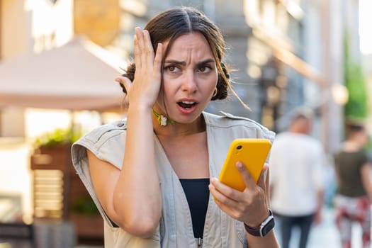 Pretty young woman use smartphone typing browsing, loses becoming surprised sudden lottery results, bad news, fortune loss, fail. Girl walking in urban city sunny street outdoors. Town lifestyles