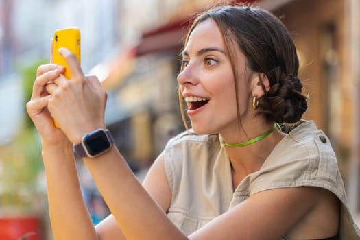 Oh my God Wow. Excited happy joyful winner pretty young woman use smartphone typing browsing celebrating win good message news. Girl with mobile phone walking in urban summer city street outdoors