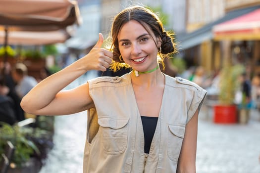 Like. Happy pretty young woman looking approvingly at camera showing thumbs up, like sign positive something good positive feedback. Girl walking in urban city sunny street. Town lifestyles outdoor