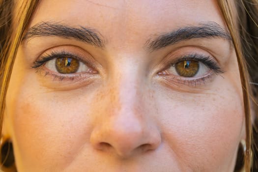 Extreme close-up macro portrait of face. Young adult beautiful pretty woman's eyes looking at camera. Brown eyes of teen girl female. Caucasian woman wide opening eyes, smiling. Laser correction
