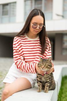 Young woman and tabby cat sitting on a bench outdoors