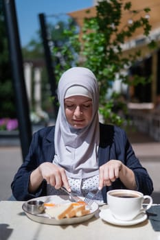 Caucasian woman in hijab having breakfast in outdoor cafe