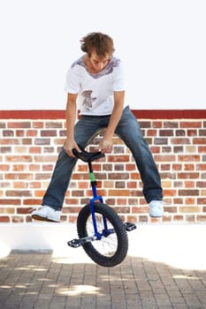 Unicycle, sports and man jumping in city for exercise, training or workout on wall mockup space. Action, cycling and performance of stunt in street for trick, travel and eco friendly transportation