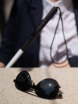 A blind woman in a business suit is sitting in an outdoor cafe