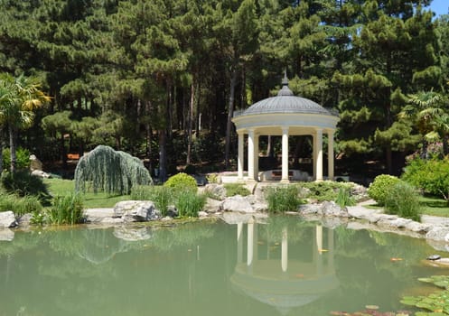 Picturesque view of the round gazebo by the fish pond, sunny summer day.