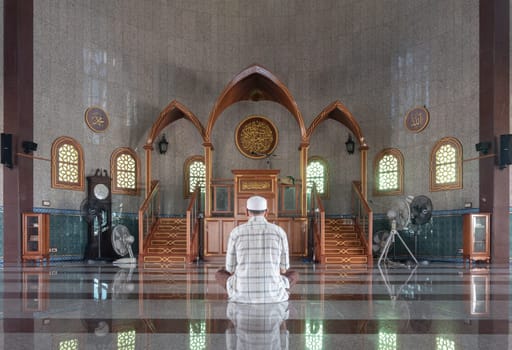 Bangkok, Thailand - June 23, 2023 - Religious muslim man sits and recite prayers for God on the floor in the Al Alawi Mosque. He prays for God in the mosque, The religion of islam, Muslim mosque, Space for text, Selective focus.