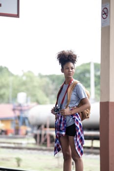 Young Asian African woman traveler with backpack in the railway train station, traveler girl walking stand sit waiting take a picture on railway platform train station. High quality photo