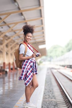 Young Asian African woman traveler with backpack in the railway train station, traveler girl walking stand sit waiting take a picture on railway platform train station. High quality photo