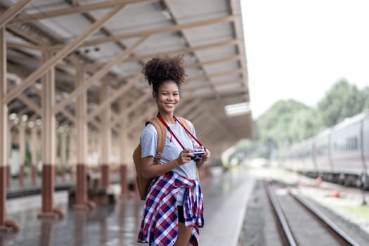 Young Asian African woman traveler with backpack in the railway train station, traveler girl walking stand sit waiting take a picture on railway platform train station. High quality photo