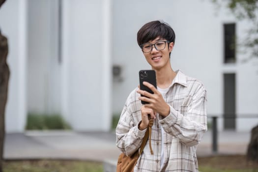 asian male college student with smart phone on sunny campus.