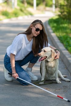 Blind young woman cuddling with guide dog on a walk outdoors