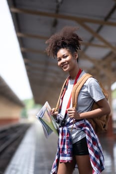 Young Asian African woman traveler with backpack in the railway train station, traveler girl walking stand sit waiting take a picture on railway platform train station. High quality photo
