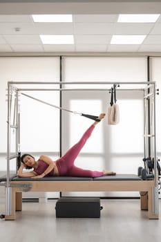 Asian woman doing pilates exercise on cadillac reformer machine