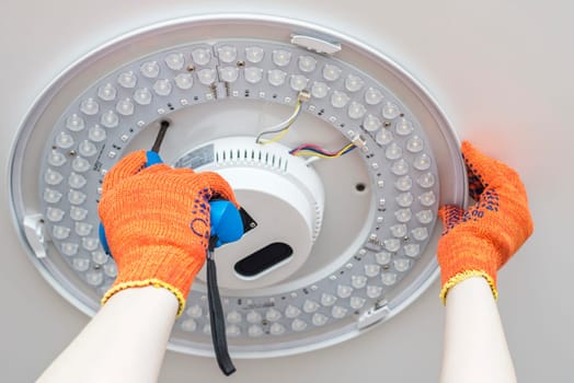 An electrician installs a chandelier on the ceiling. Hands of an electrician installing and connecting a lamp to a ceiling.