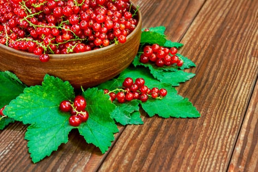 Bowl of freshly picked redcurrants and leaves on a table. Fresh redcurrant berries in the bowl on wooden background