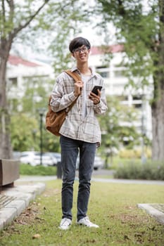 asian male college student with smart phone on sunny campus.