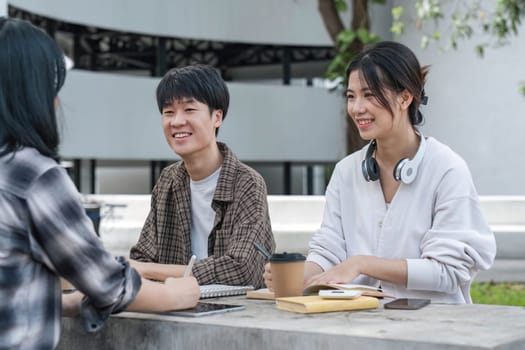 Group of Student working on laptop and record in book together at university. Happy friend successfully completes the thesis report and passed the final exam in asian college...