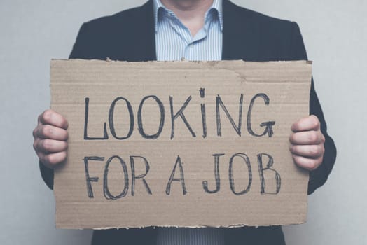 A young businessman who lost his job due to quarantine is looking for a job. A businessman holds a cardboard sign with the text LOOKING FOR A JOB. Unemployment growth concept
