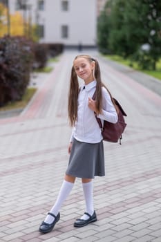 Caucasian girl in uniform and with a backpack goes from school